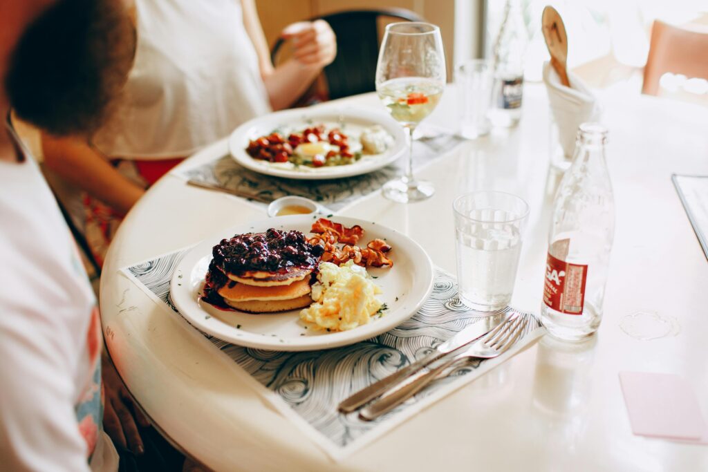 A sunny breakfast scene with pancakes, fruit, and beverages on a dining table.